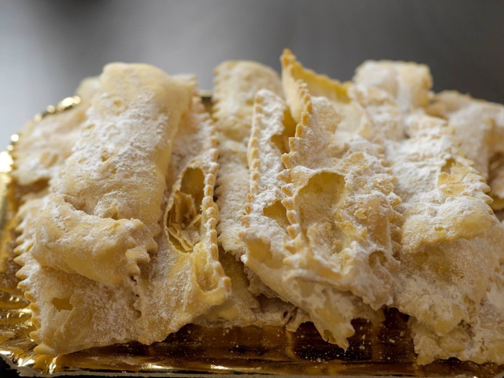 Wafer-thin, crumbly and off-white chiacchiere. They're rectangular with zig-zag edges and a sprinkling of powdered sugar.