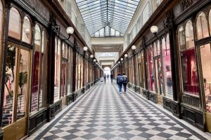 Looking down a gallerie: checkerboard floor, wood-framed shops on either side, a glass roof.