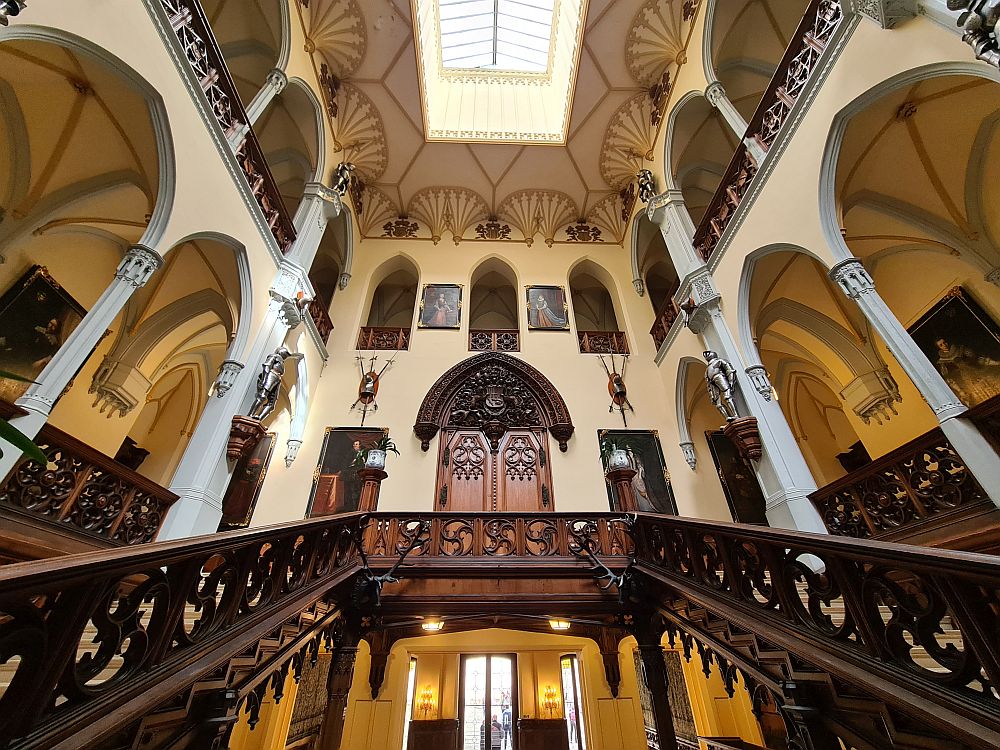 A stairway on both sides, and a very high room with arches on both sides, decorated with armor and other such items on a white background.