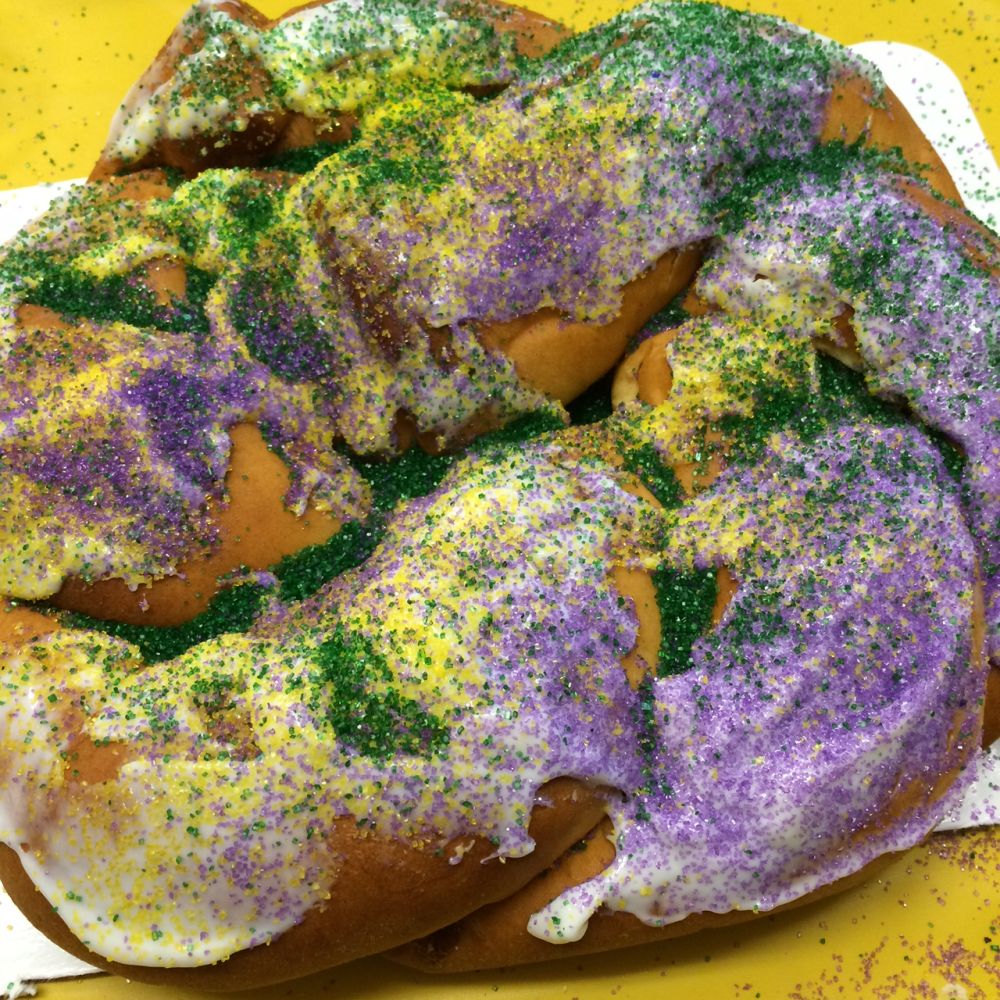 The pastry is bumpy but barely visible since it is covered with a yellow glaze that, in turn, is topped with dyed-sugar sprinkles in purple and green.