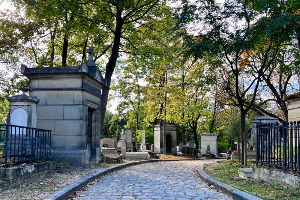 A cobblestone road curves ahead to the right, with various sizes and shapes of tombs in white stone blocks along it.