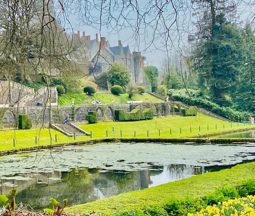 A stately home in the distance, quite large, with lots of chimneys. In the foreground, a green park with a small pond.