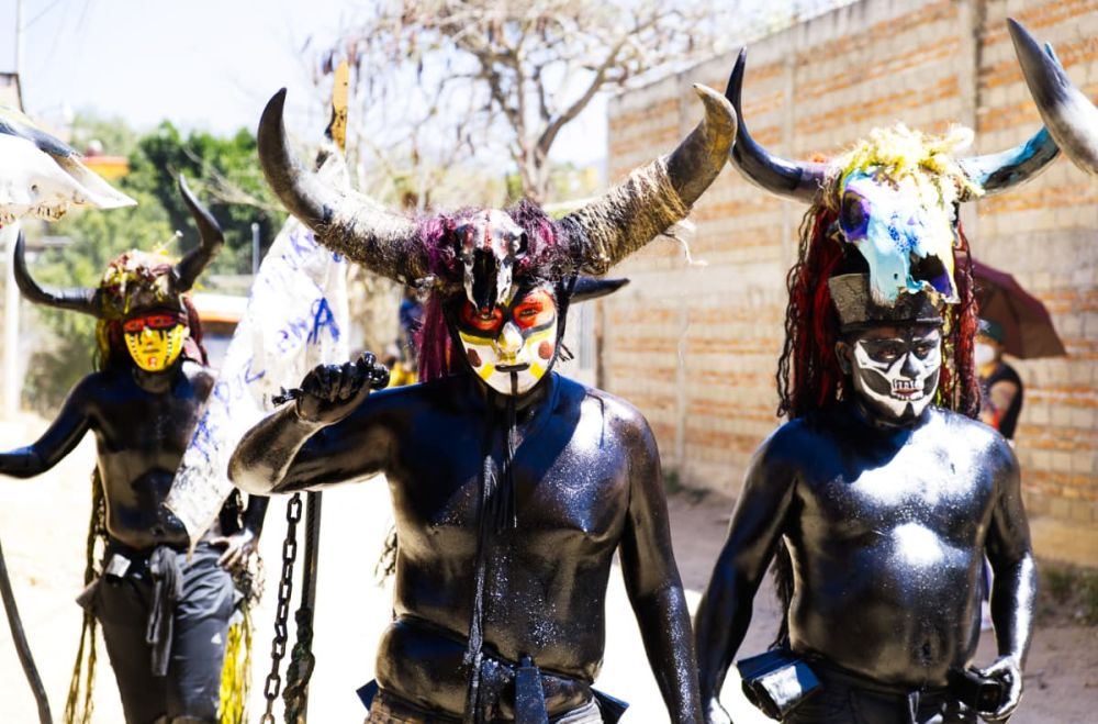 Men covered in black oil, with painted-on face masks of white and red and black and large cow horns on their heads at Oaxaca carnaval.