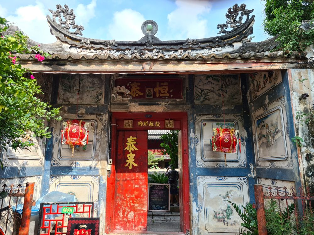 An ornate gateway with carved peak and the walls covered in paintings, all of it in decay.