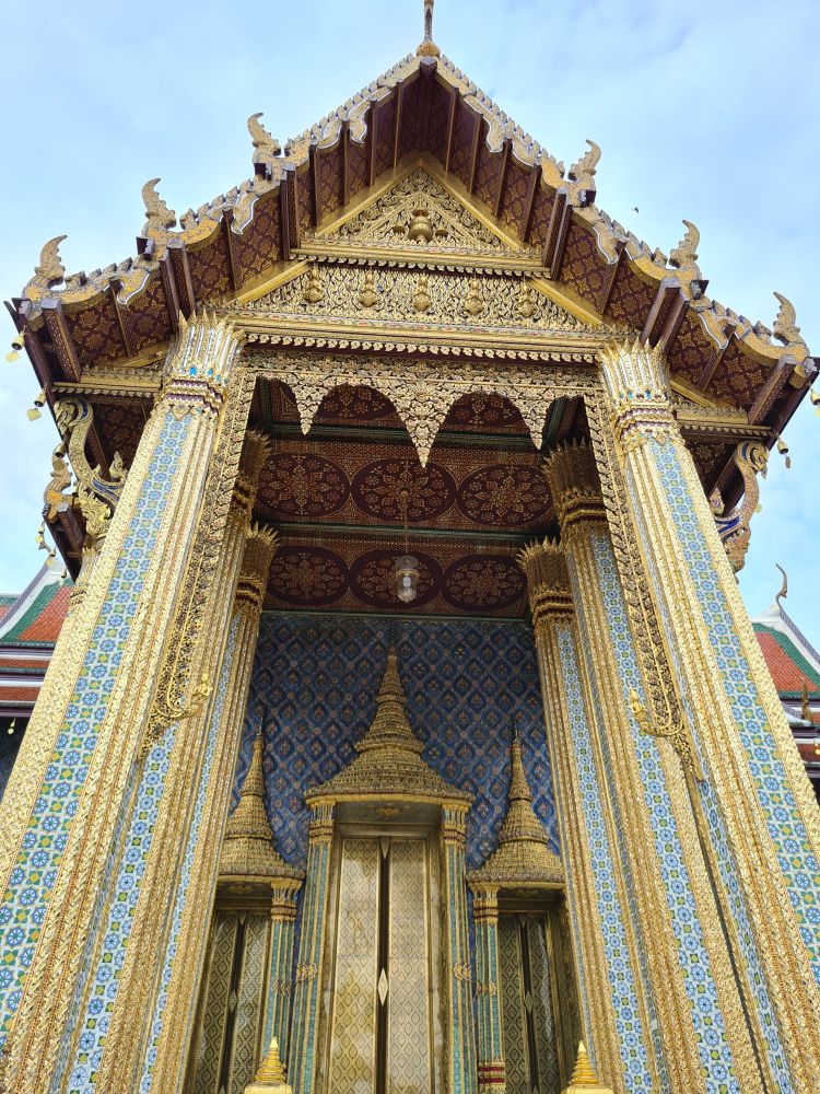 Looking up at an extremely ornate temple, every inch of its gables, eaves, walls doorways and columns covered with tiling or gold detailing.