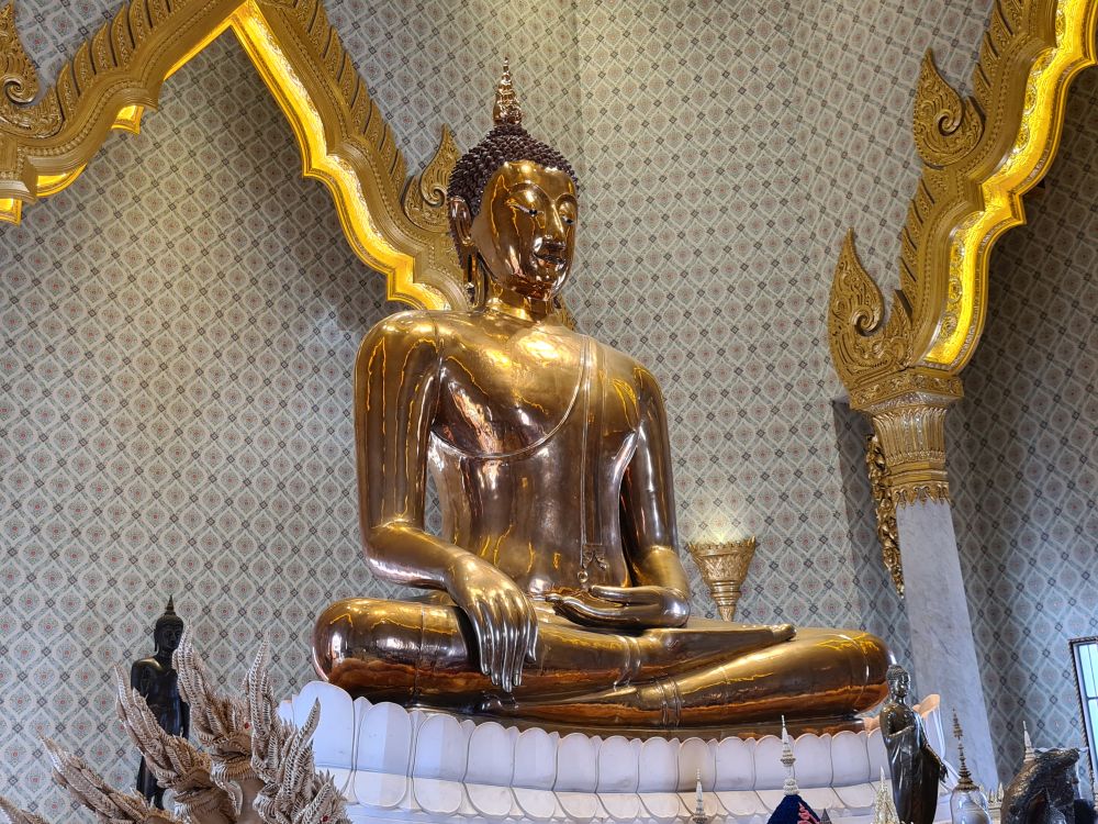 Shiny gold Buddha in Sukhothai style in the Subduing Mara pose.