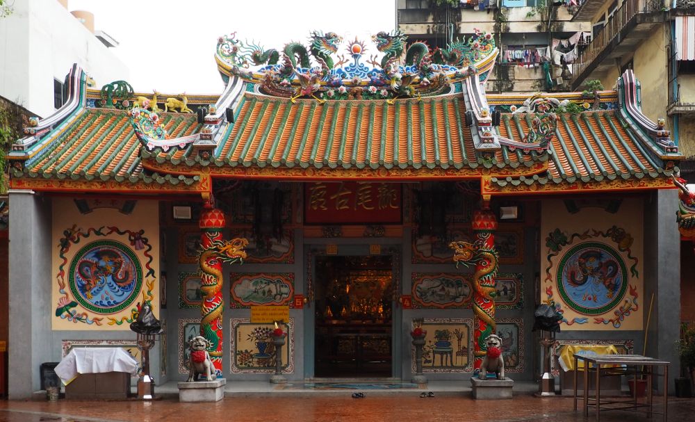 A very colorful single-story temple with typical Chinese roof shape and a complicated carving along the roof's peak.