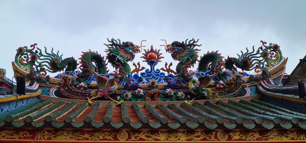 The ornate sculpture on the roof of the Leng Buai La Chinese Temple in Bangkok: colorful images of two dragons and two roosters with lots of further embellishments.