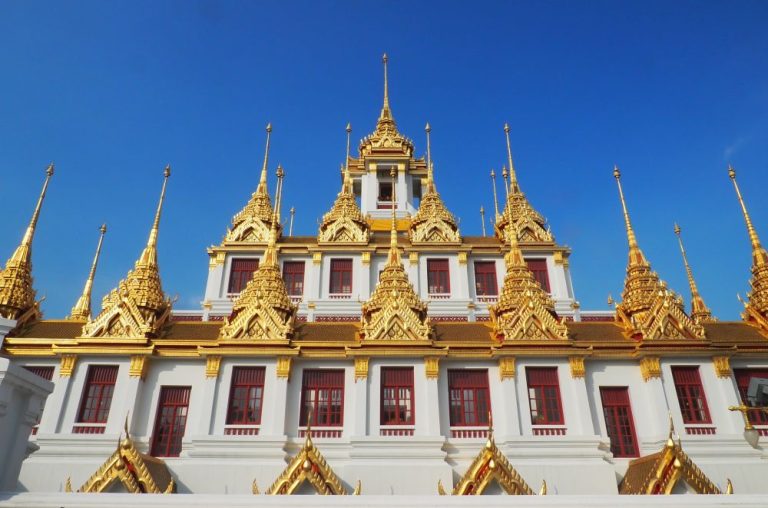 Looking up at the Metal Castle temple in Bangkok: white walls, golden spires.
