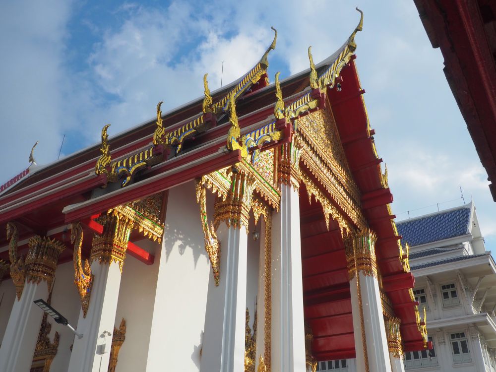 Looking up at the front of a temple but seen from the side: a highly decorated gable in shiny gold and red paint.