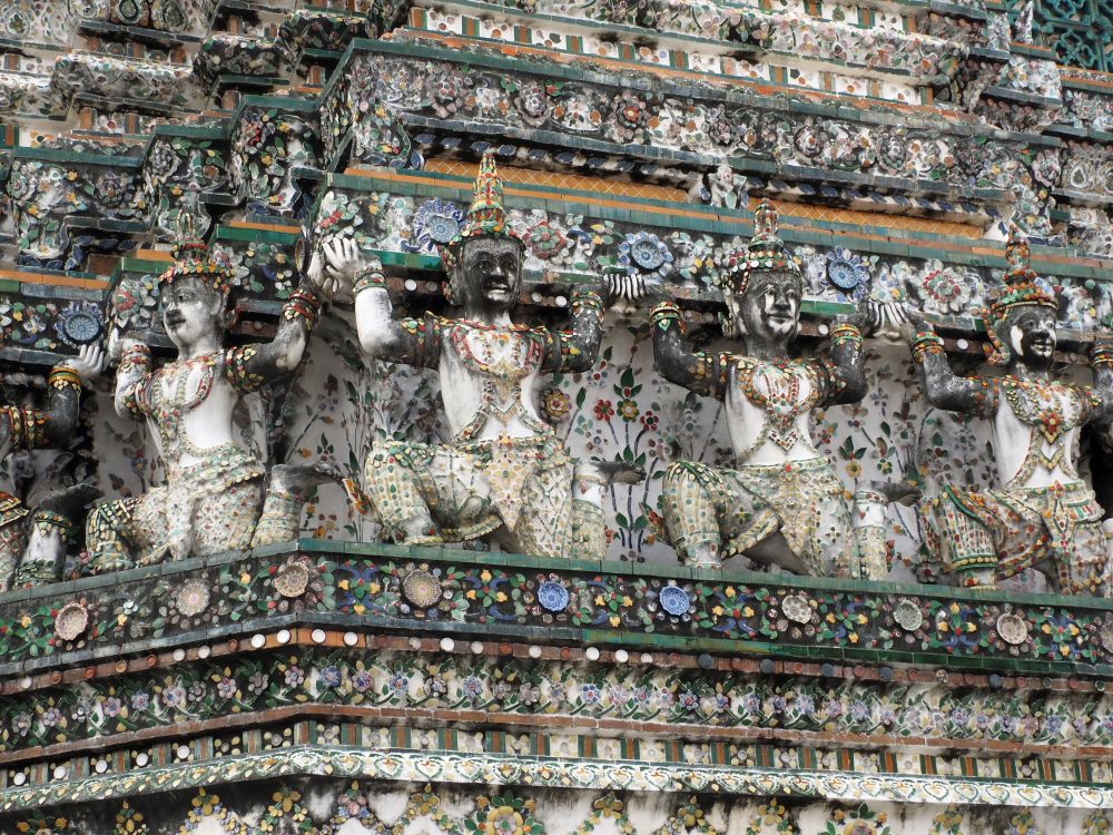 One of the tiers of the stupa is lined with human-like figures, on one knee and with the other knee up, arms up as if supporting the tier above them. They're all wearing ornate hats and their clothing is decorated with ceramic tile.