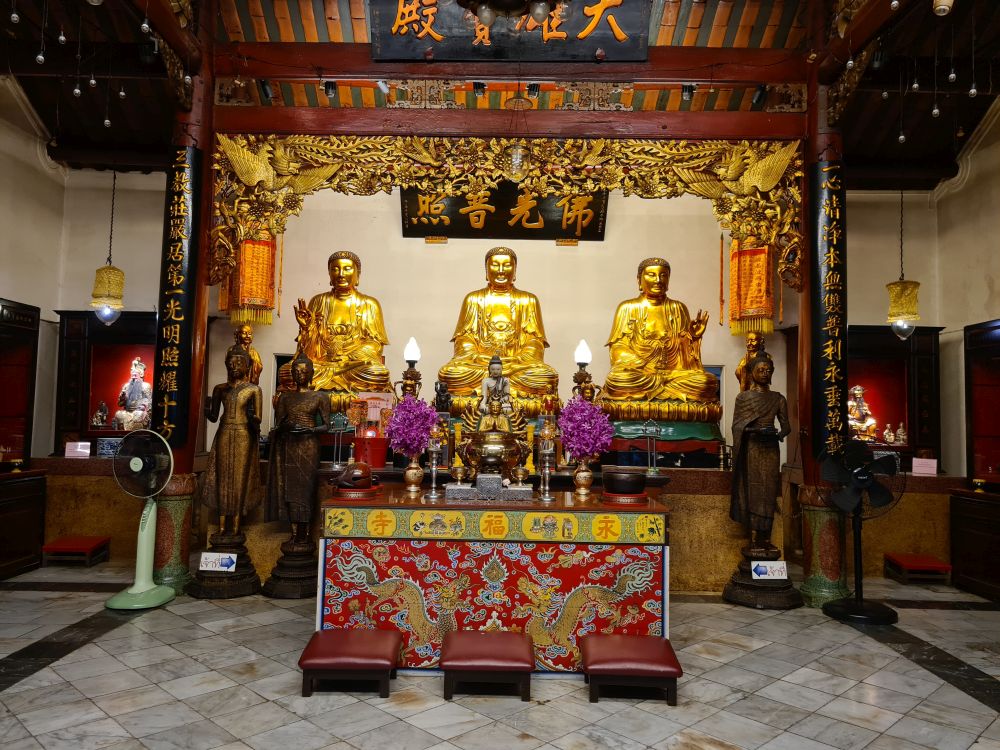 View of the altar at Wat Bamphen Cin Phrot: 3 sitting golden Buddhas, with smaller standing Buddhas in front and beside them.