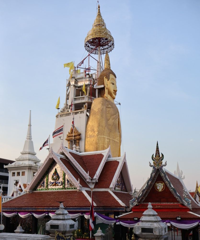 A temple roof visible in front, a towering golden standing Buddha behind it.