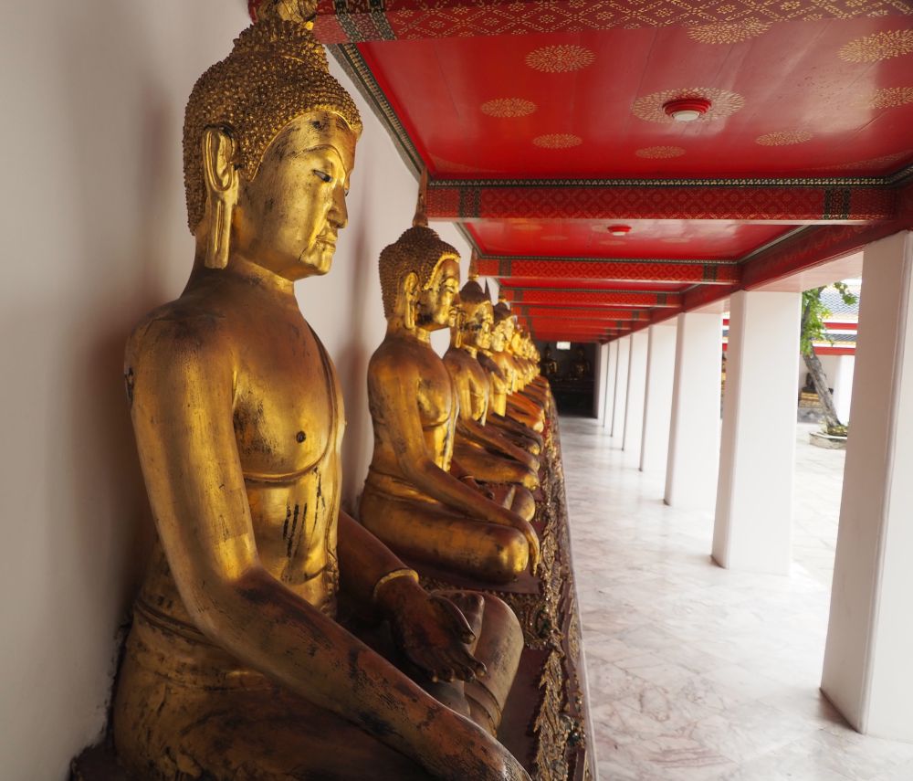 Looking down a row of gold-colored seated Buddhas in the Subduing Mara pose.