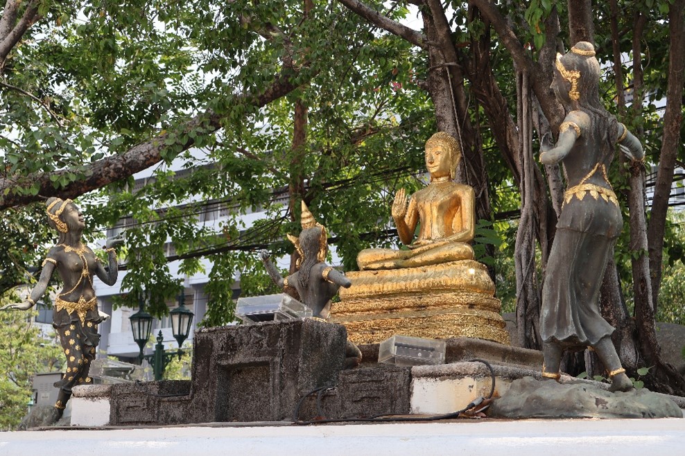 A golden sitting Buddha witth other standing figures looking at him.