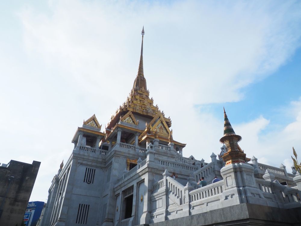 Looking up at a white temple with gold-painted spires.