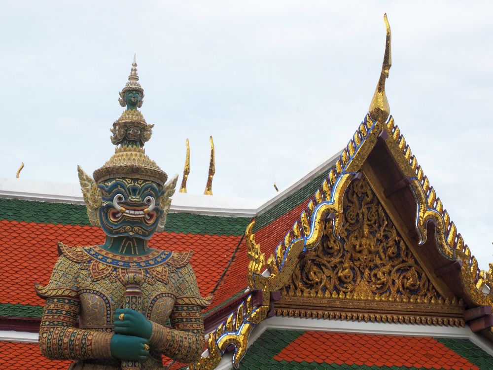 A Taksha in many colors, with a fierce face, next to a very shiny gold gable over an entrance.