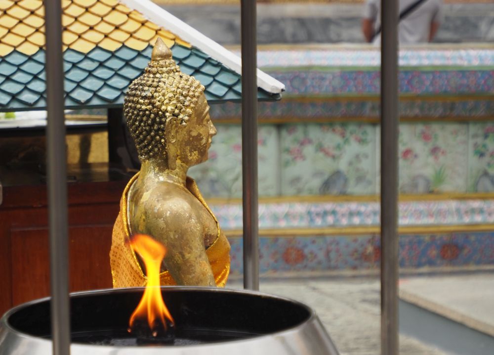 Side view of a Buddha statue with flame in front of it.