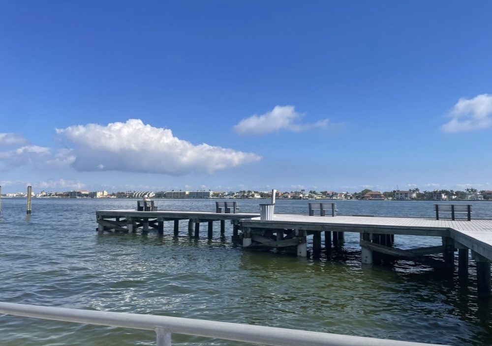 Just a simple pier: wooden boards on piles extending in a zigzag shape over the water. Buildings visible far away across the water.