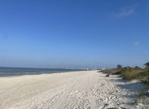 Long stretch of white sand with no one on it and dunes on the right.