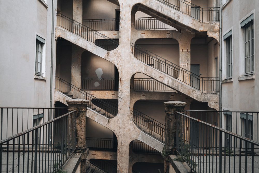 Several floors of the stairway show in the photo, all going upwards to the left, with level walkways linking along the building to the beginning of the next flight. The stairs look like concrete, with a metal railing.