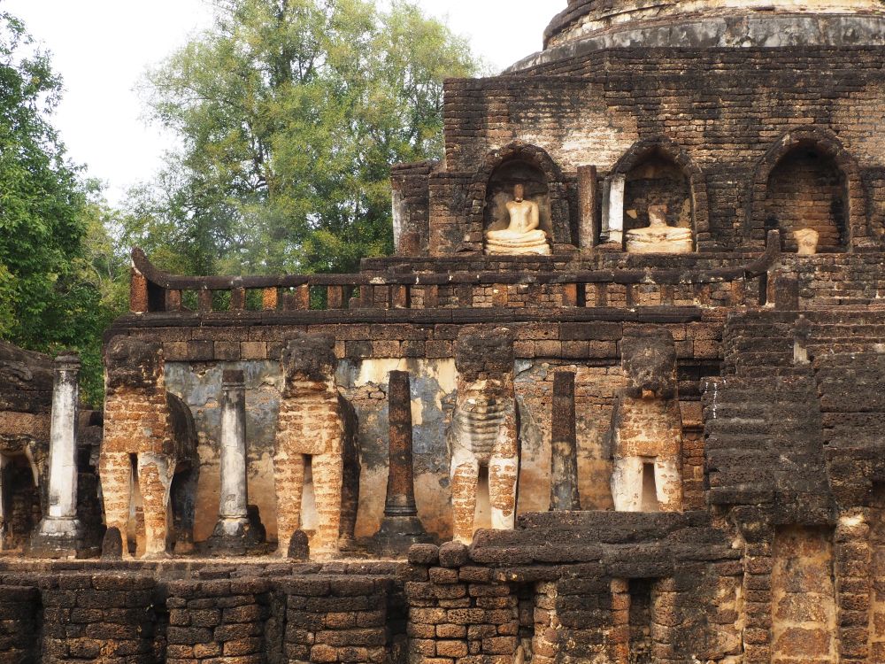 The stupa has a series of layers like a wedding cake. Around the bottom layer, the remains of a row of elephants. On the next layer up, the niches have seated buddhas.