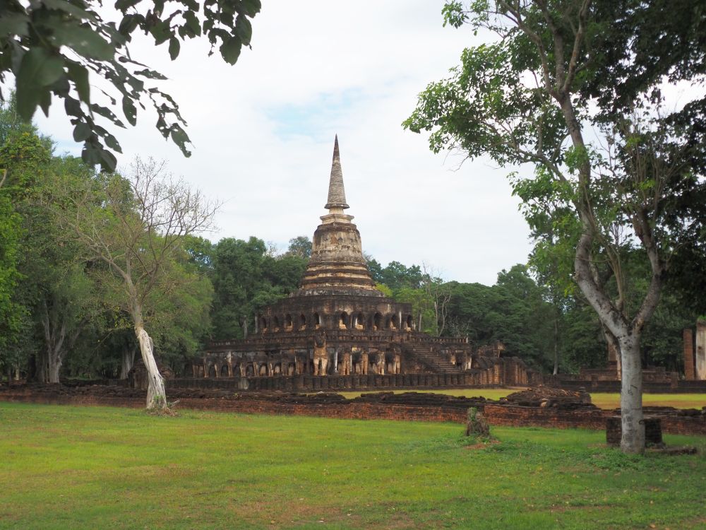 A view of the temple Wat Chang Lom across a field. It has a square base that tapers up to a pointed tip.