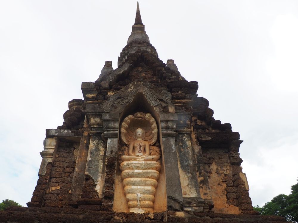 In a niche on the side of an ornate stupa that tapers to a point: a statue of a Naga Buddha on a coiled snake, with snake heads curved over his head.