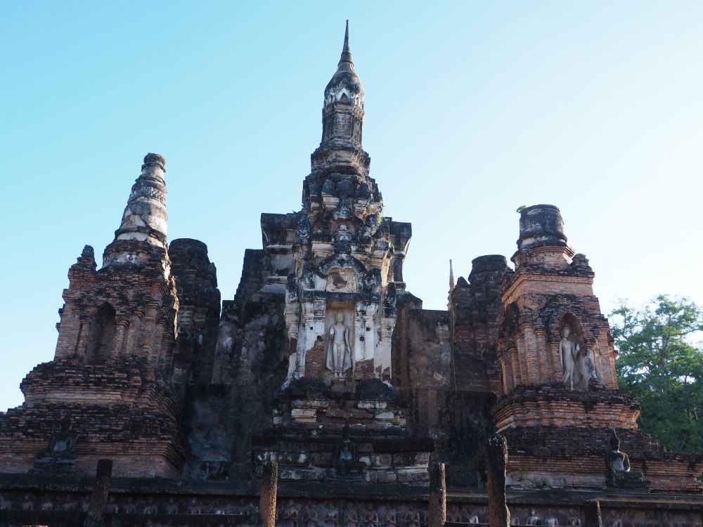 The photo shows 3 stupas close together. The central one is the most complete, with carved details and a point on top.