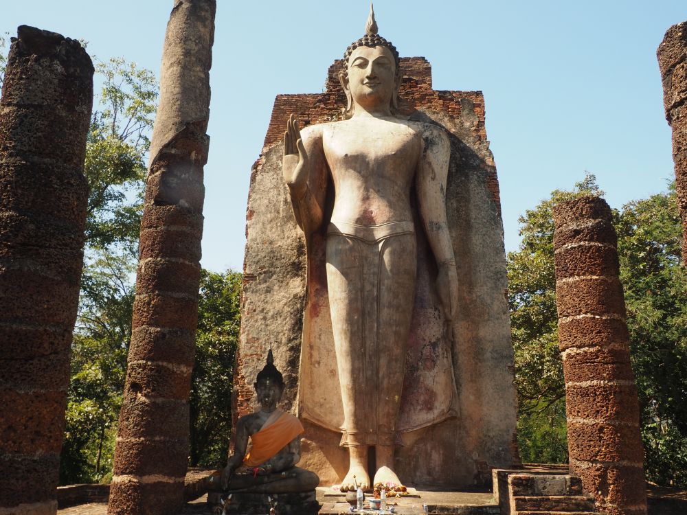 The Buddha statue stands against a wall, right hand from the elbow, palm out. In front of it, a small (human-sized) sitting Buddha in Subduing Mara pose.