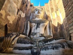 large Buddha statue, sitting in Subduing Mara pose, enclosed by walls very close by and only a bit taller than the statue is.