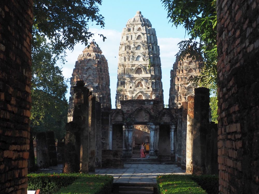 Looking though a gateway and down a path at the end of which are three prangs: towers with 7 layers and rounded tops.