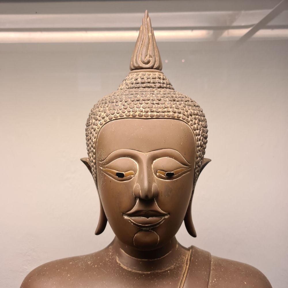 Sukhothai Historical park museum statue with typical Sukhothai style flame on the top of the head and curly hair, but with an unusual eye design.