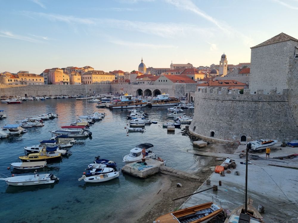 The old harbor of Dubrovnik: the city walls edge the harbor, where various small boats are moored.