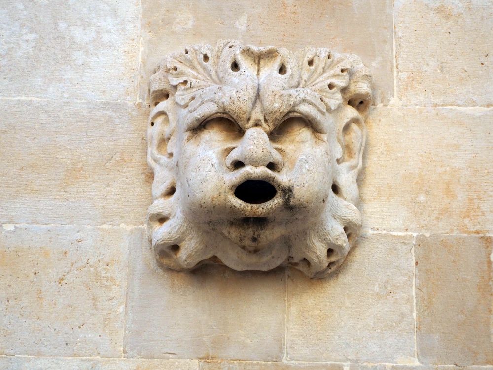 A funny carved stone face with a mouth that looks like it's about to spew.