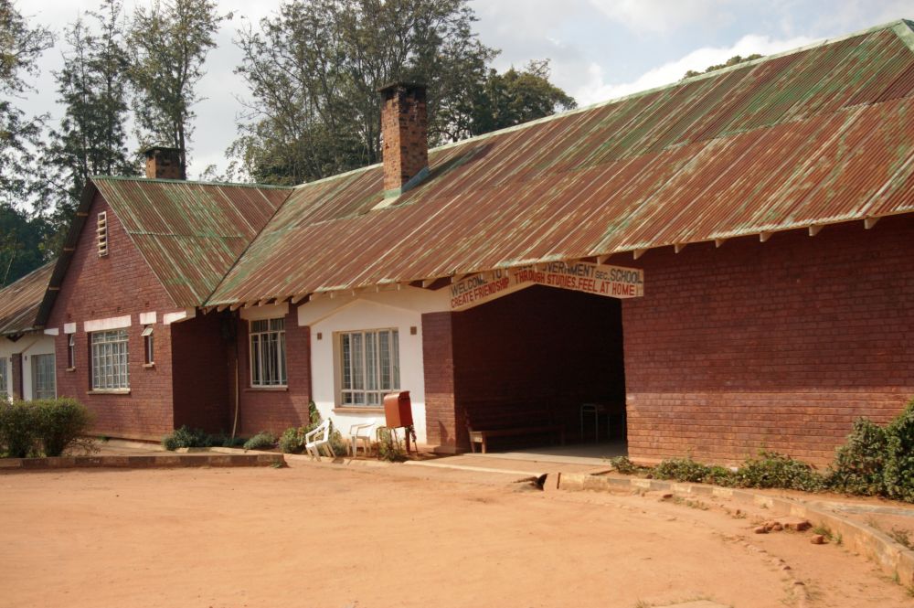 A single-story building in red brick - this photo only showed the archway entrance and a few windows next to it. A sign over the archway reads: "Welcome to Mzuzu Government Sec. School Create Friendship Through Studies. Feel at Home.