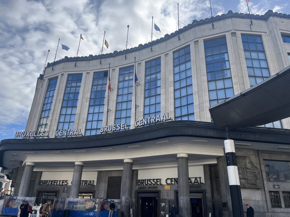 A large building in a rather deco style, with large glass windows up the front and pillars holding up a portico across the front.