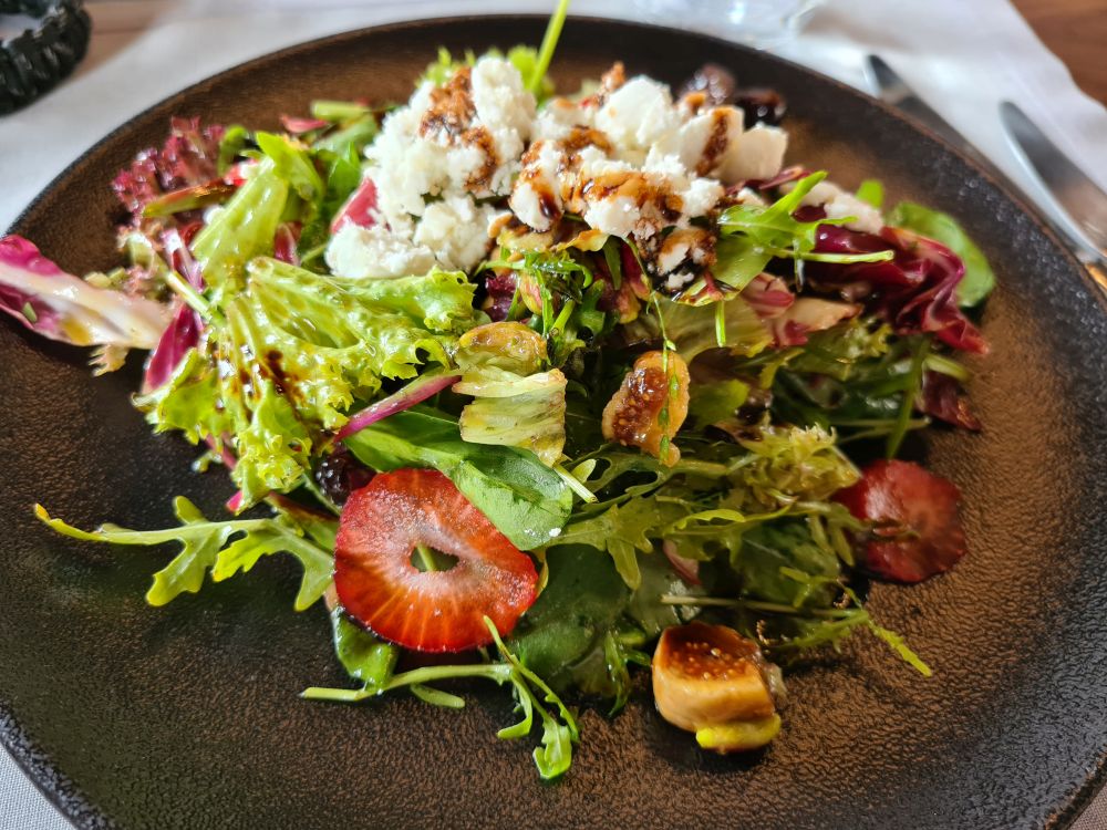 A green salad with slices of strawberry and crumpled white cheese.