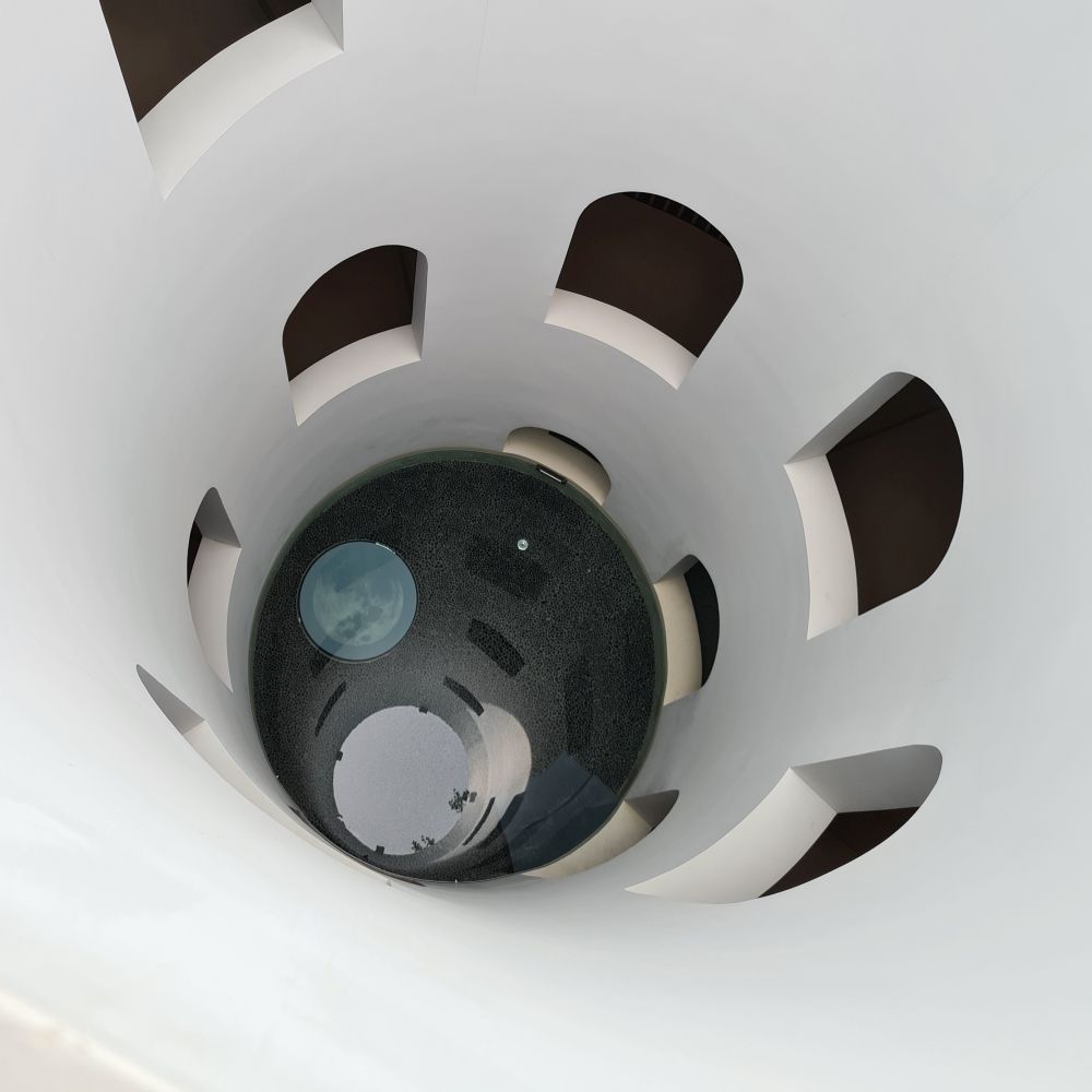 View down the waterwell in the Euphoria Retreat spa: a cylindrical tube, painted white on the sides with a row of windows spiraling around it - water at the bottom.