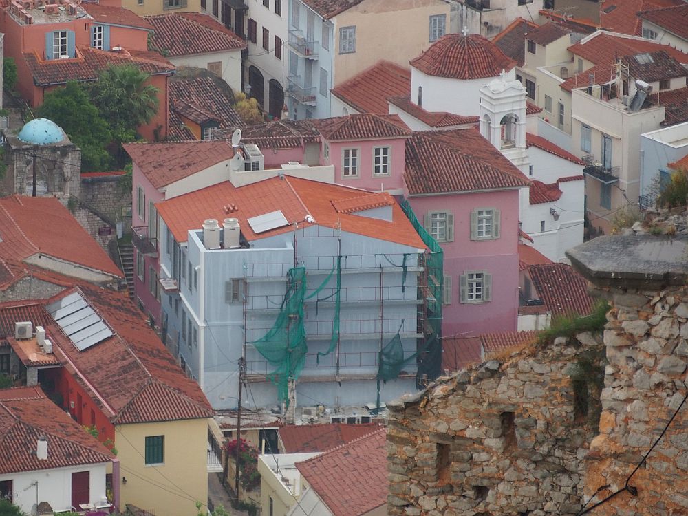 View from above of a cluster of buildings: one is covered with scaffolding, the one next to and behind it is painted pink, and a white church peeks from behind that.