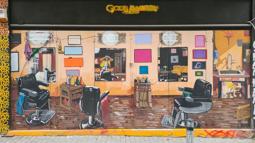 A large wall of street art showing a barbershop, with mirrors on the far wall, including one showing a person taking a photo of the street art!