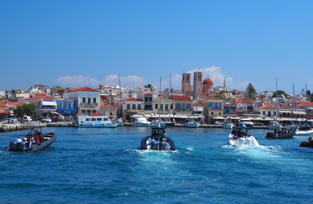 A crowded port with lots of buildings close together along the water and behind them, and several motorboats heading toward the port.