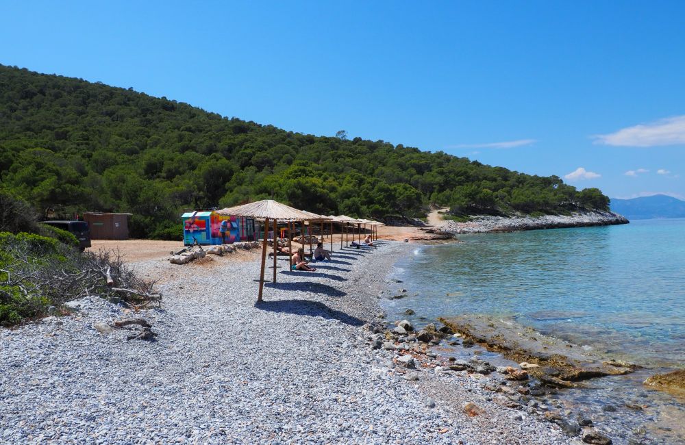 A single row of round thatched sun shelters along a sandy beach with very few people on the beach.