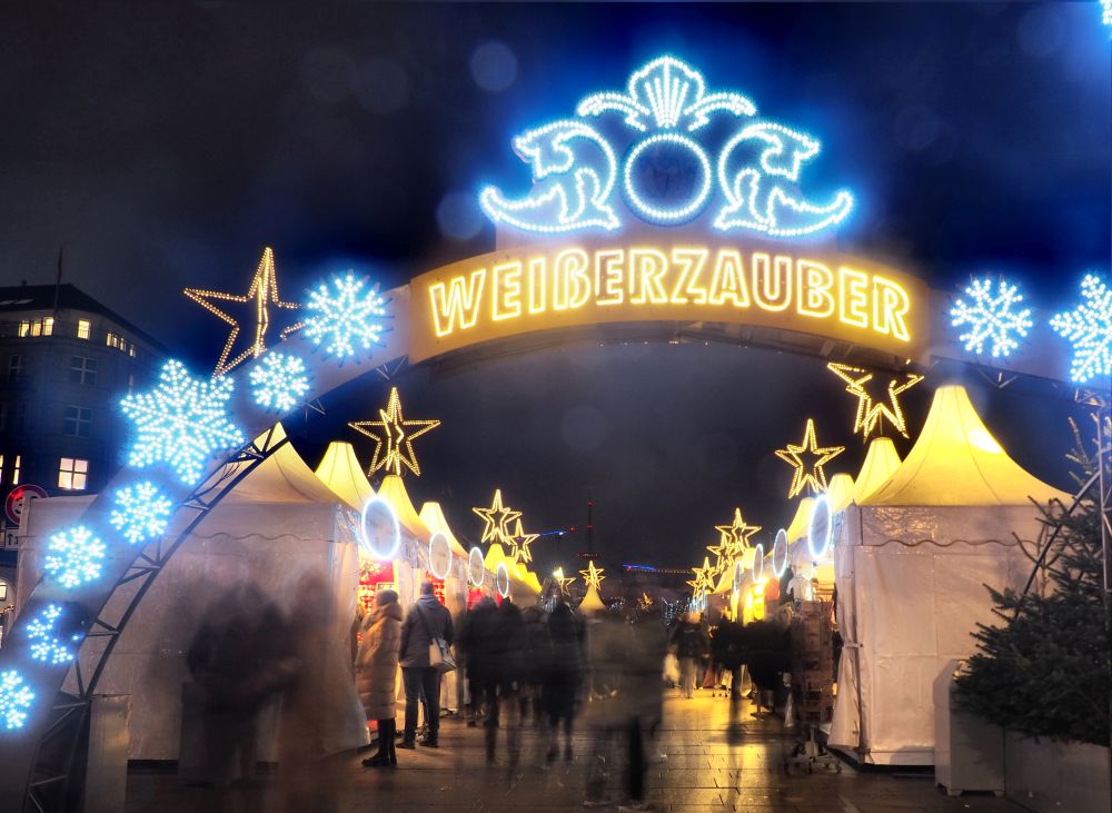 The archway at the entrance to the market is lit up in white and blue, reading "Weisserzauber."