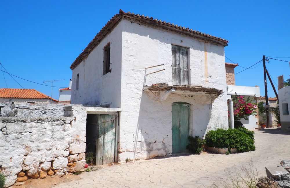 A two-story house of white-painted stone, with a single wooden door in the center of each story, and a small balcony at the upper door.