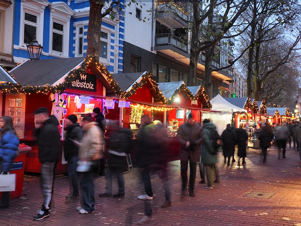 Red market stalls edged with lights, and many people (blurred) in front of them.