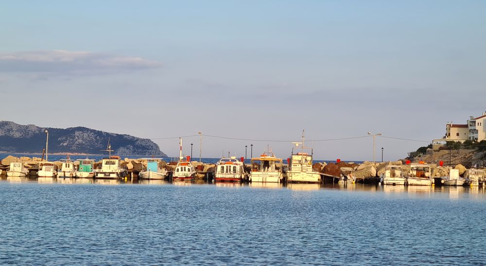 Looking across water at a small fishing boats lined up along a long pier.