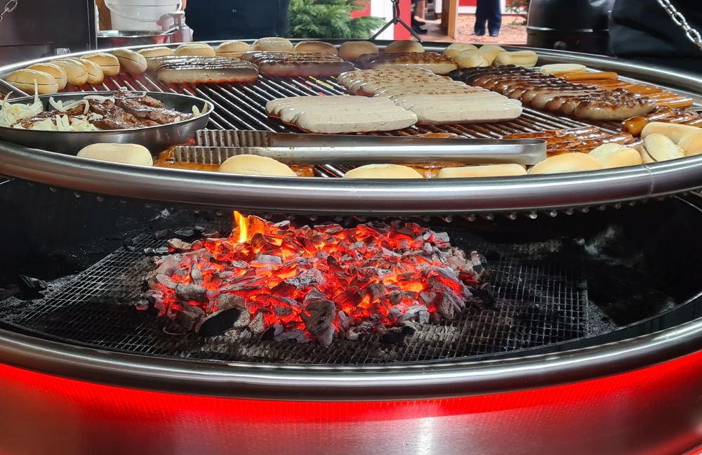 A huge round barbeque: below is a neat pile of red-hot coals. A large round grill above that with LOTS of sausages of various kinds, plus rolls around the edges.