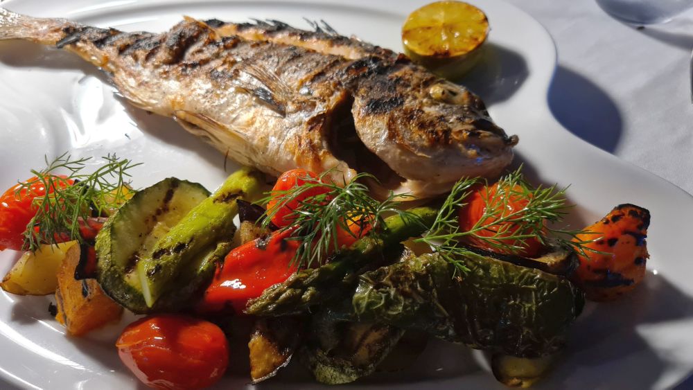 A whole grilled fish with a side of mixed vegetables.