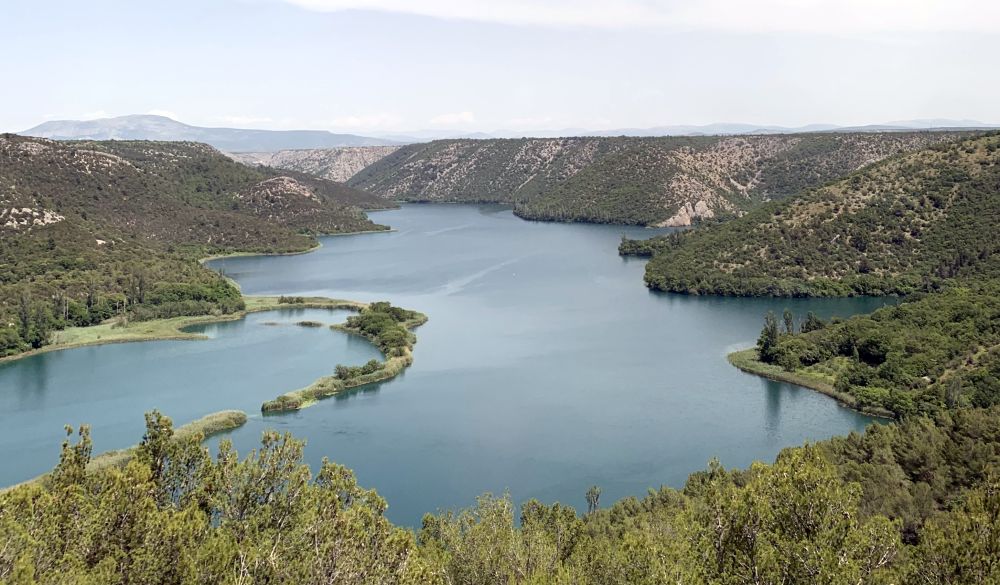 View over a large lake in Krka National Park in Croatia, surrounded by low hills covered in green shrubbery.